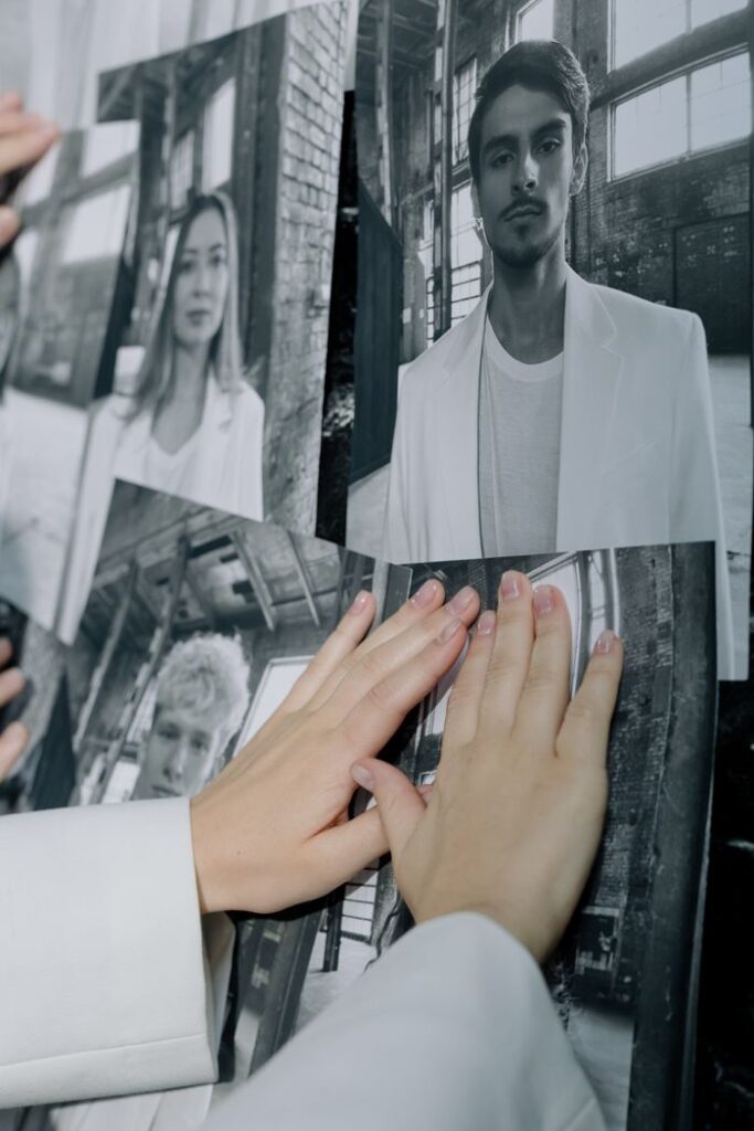 Close-up of hands arranging black and white portrait prints on a wall indoors.
