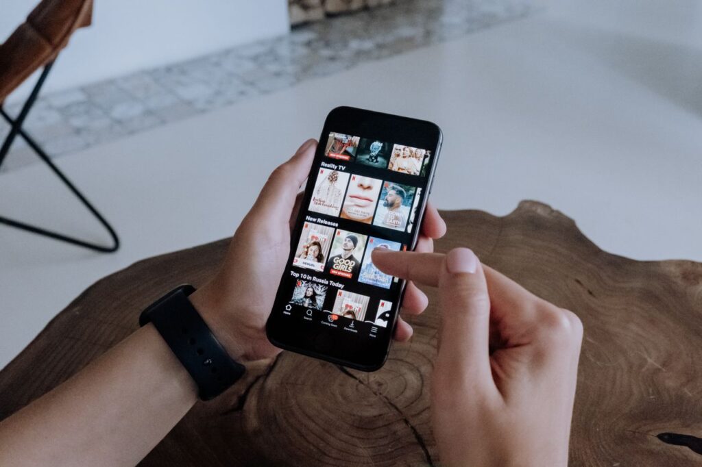 A person using a smartphone to explore and select shows on a streaming platform indoors.
